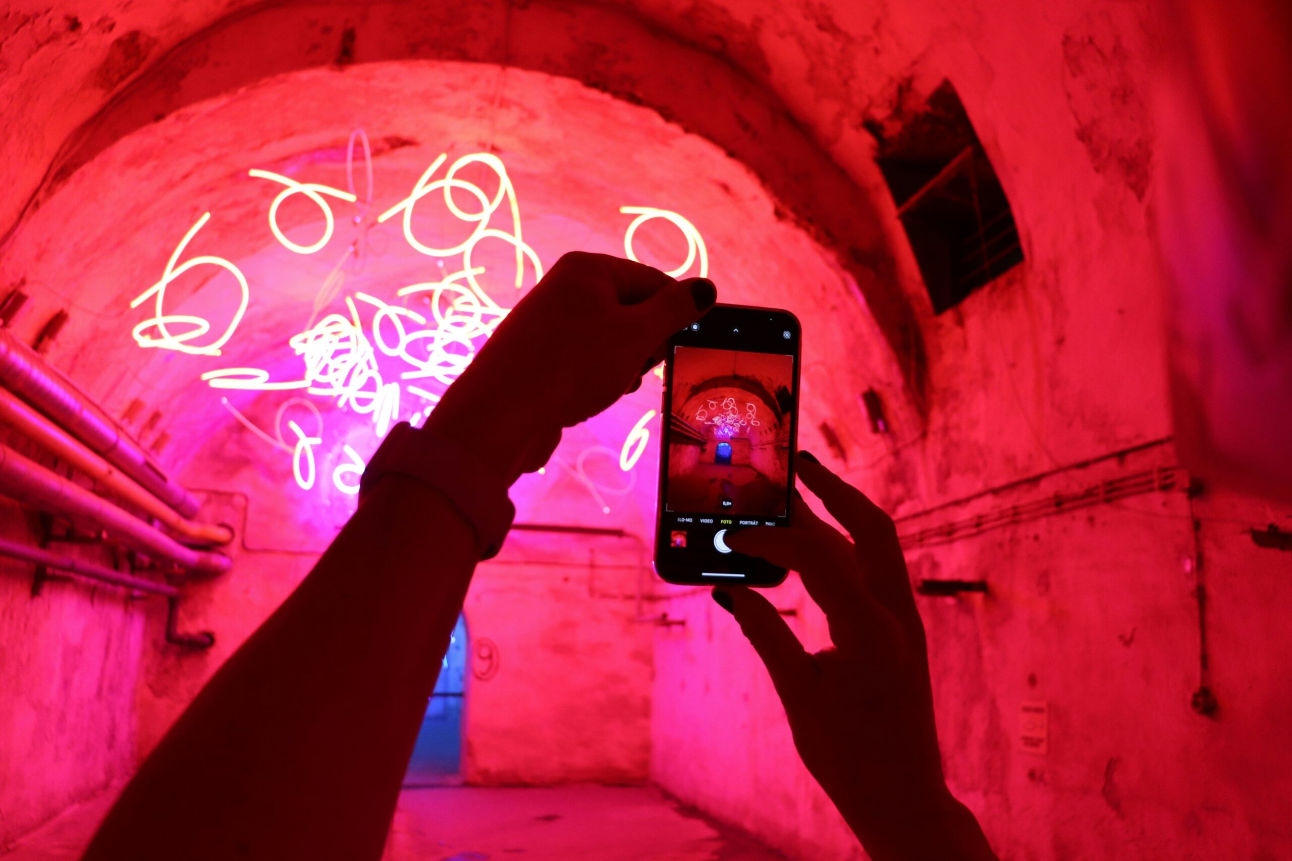 Smartphone, das Bild von einem Tunnel mit roten Lichtröhren macht. Emotional aufgeladenes Bild.