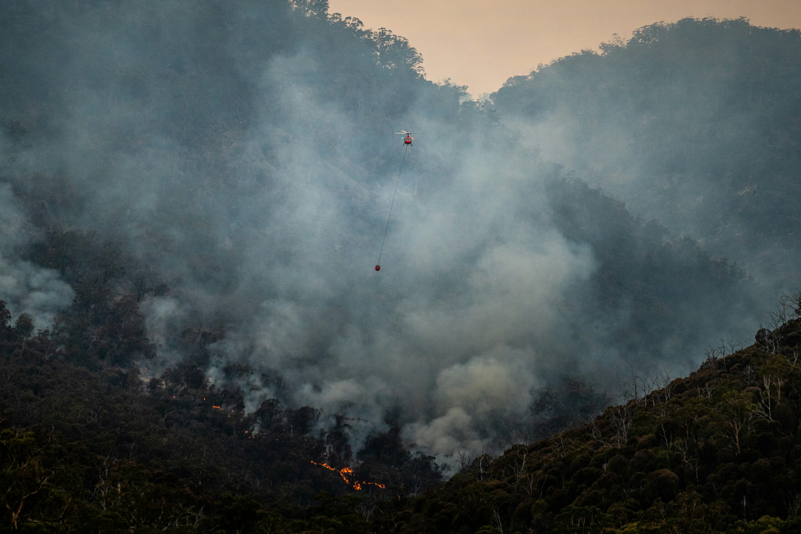 Wald mit Rauch und 2 Helikoptern, die auf den Zuseher zufliegen.