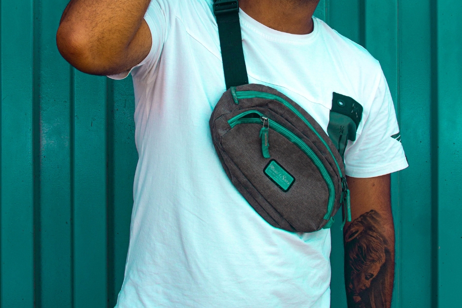 Bauchtasche in grau und grün, junger Mann mit Tattoos und weißem T-Shirt