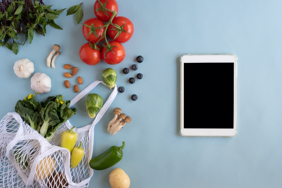 Tomaten, Früchte, Gemüse, Pilze, Tasche und Tablet auf blauen Hintergrund