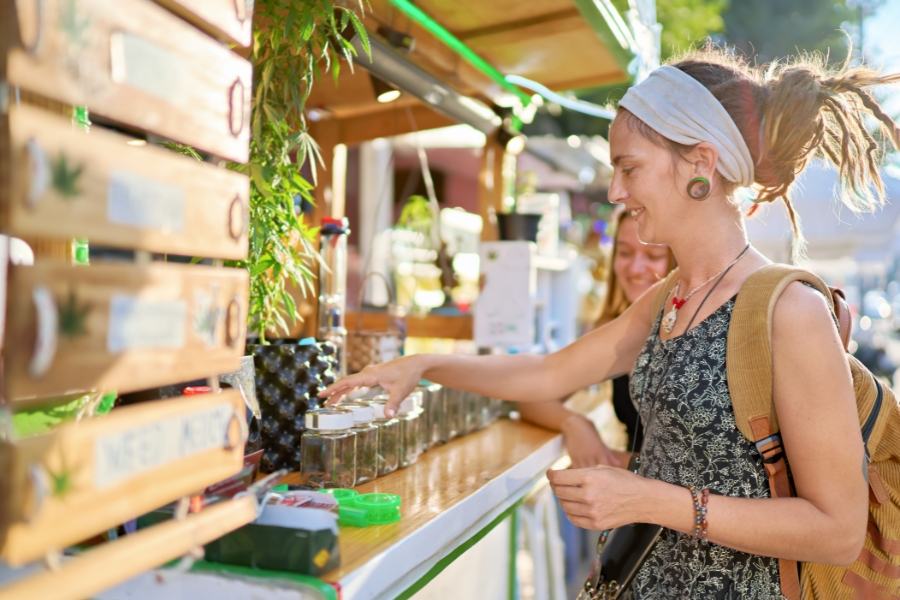 Cannabis Stand mit verschiedenen Sorten, Frau sieht die Blüten im Glas an