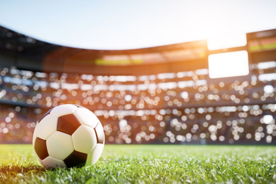 Ein Fußball auf dem Rasen eines Stadions, welcher von der Sonne beschienen wird.